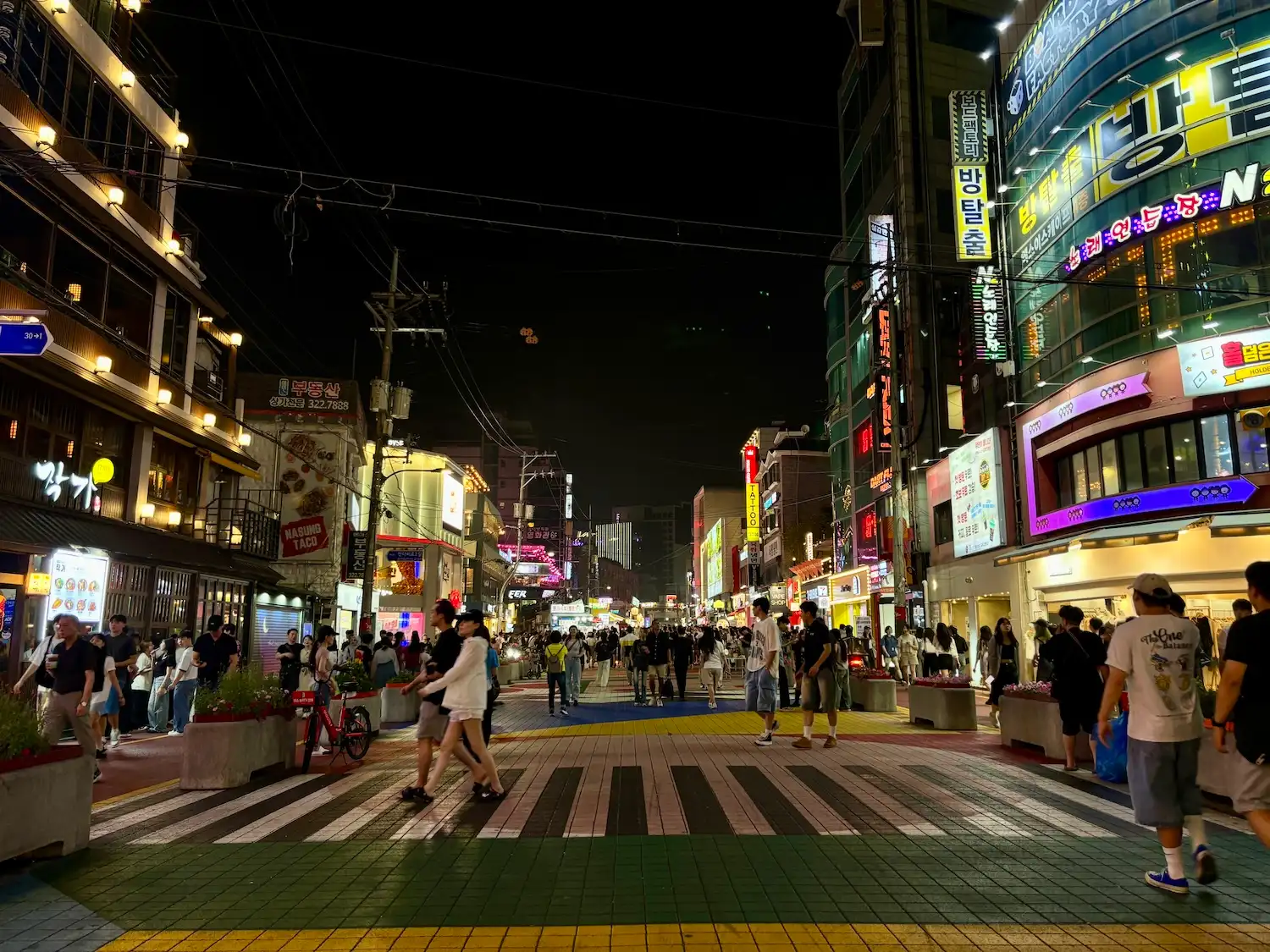 A lively street in Hongdae at night, filled with people enjoying the nightlife.