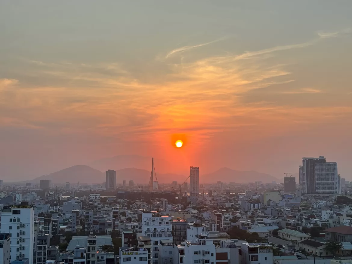 Da Nang, Vietnam city skyline during sunset. One can see mountains, high-rises, and an orange sun set